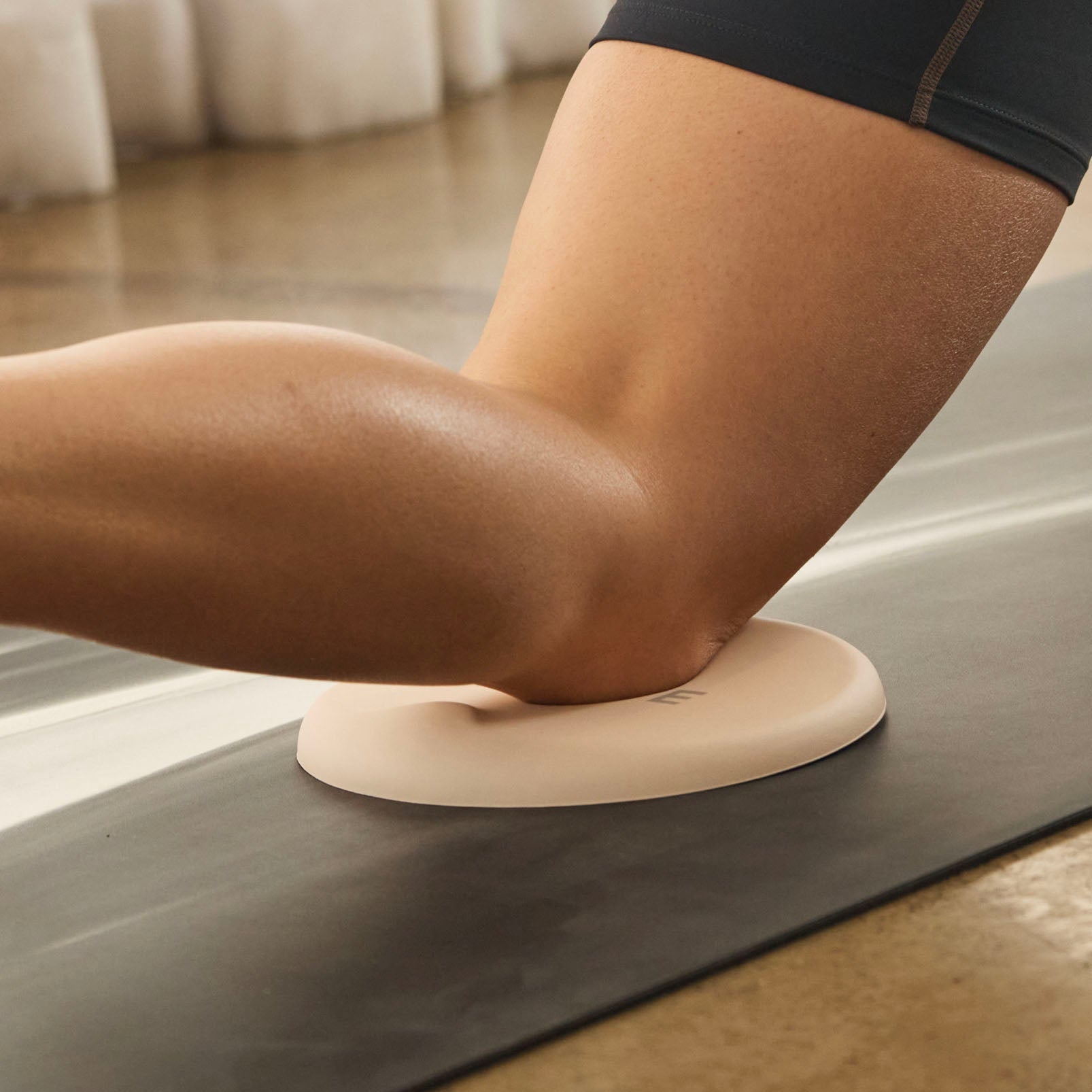 A woman holding a leg pose. She is wearing black shorts and is using a knee pad for support.